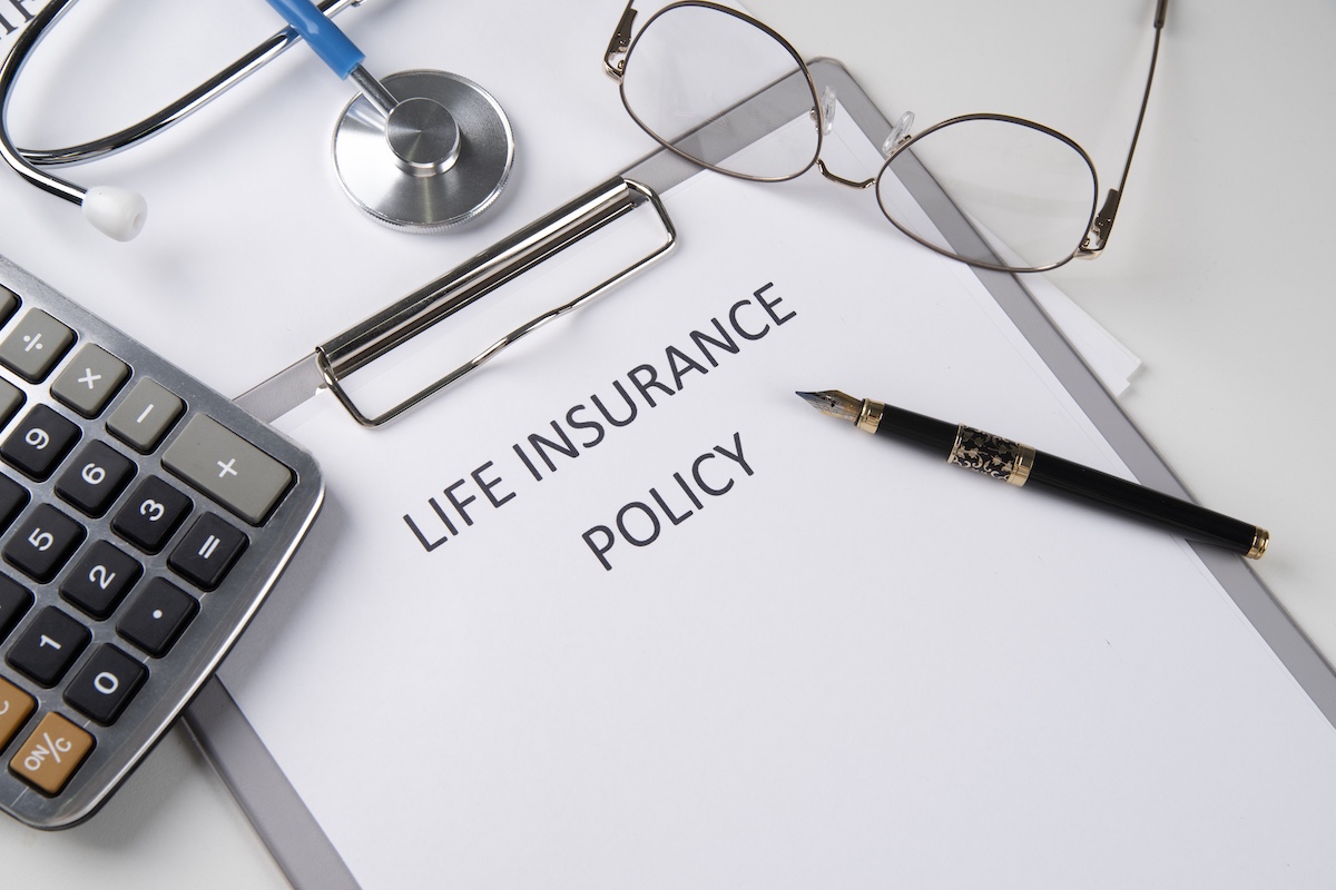 Life insurance policy document on a clipboard with a calculator and reading glasses nearby.
